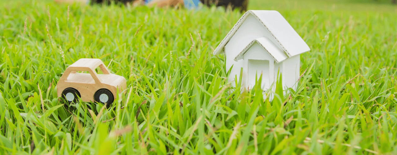 photo-of-a-wooden-toy-car-and-a-white-paper-house-on-grass